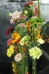 Colorful flower arrangement featuring a mix of vibrant blooms including gerbera daisies and carnations in a sleek modern vase, creating a lively and refreshing display.
