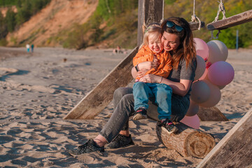 A young mother with her daughter little child with balloons by the sea with a beautiful landscape
