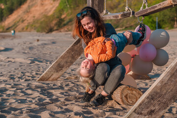A young mother with her daughter little child with balloons by the sea with a beautiful landscape