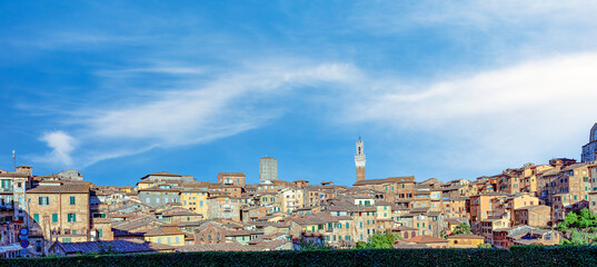 View of medieval Siena showcasing charming buildings with terracotta roofs, elegant towers, and a clear blue sky, offering a glimpse of Italian history and architecture.