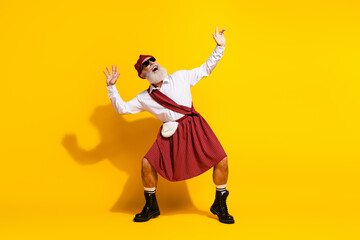 Confident elderly man in traditional Scottish attire posing energetically against a vibrant yellow...