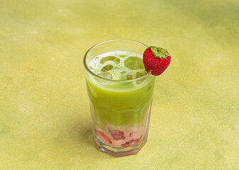 Refreshing iced matcha latte blended with strawberry puree and ice cubes, garnished with a fresh strawberry, served in a tall glass against a vibrant green background