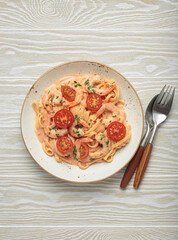 Seafood linguine pasta in creamy sauce with shrimp and cherry tomatoes, garnished with fresh parsley, served on white wooden background with cutlery top view