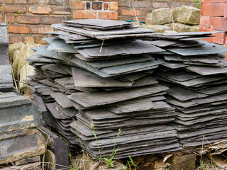 Stack of gray slate tiles against a brick wall in an outdoor setting.