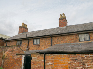 Rustic brick house terraced with chimney stacks under a cloudy sky.