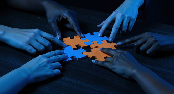 Multiple hands assembling blue and orange puzzle pieces on dark surface. Team collaboration connecting jigsaw parts together. Problem solving concept. Business consulting, team building services - Powered by Adobe