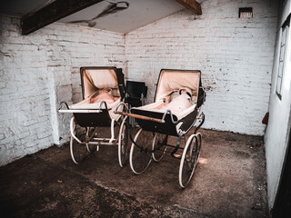 Vintage prams in an old brick-walled garage evoke a nostalgic atmosphere.