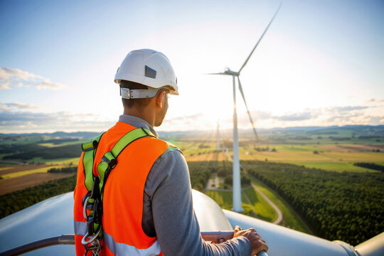 Wind turbine technician inspecting a wind farm at sunset, renewable energy concept
