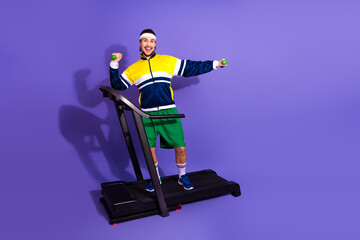 Young man in retro sportswear exercising on a treadmill with dumbbells on a vibrant purple background