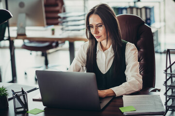 Obraz premium Confident businesswoman working on a laptop at her office desk, showcasing focus and professionalism in a corporate environment