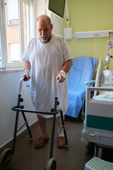 Senior man with injured leg using walker in hospital room, recovering from surgery