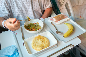 Hospital patient eating a healthy meal of green beans, spanish omelette and banana, served on a...