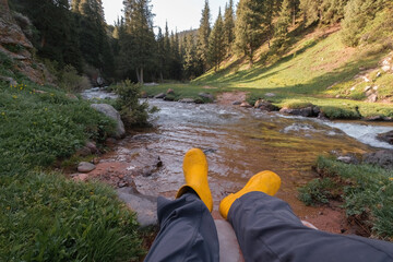 Female legs against the backdrop of a beautiful mountain meadow in summer with rocks, a fast river, forest and rocks, first-person view POV. 