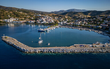 Naklejka premium Aerial view of Agii Apostoli, Greece – a serene coastal village with whitewashed houses, fishing boats, and deep blue waters framed by rolling hills and warm Mediterranean 