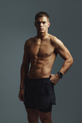 Fototapeta premium Muscular male athlete confidently posing shirtless in a studio, showcasing strength and fitness in athletic shorts. The scene highlights physical endurance and a commitment to an active lifestyle
