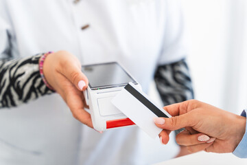 Customer engaging in a contactless payment process using a credit card on a pos terminal while...