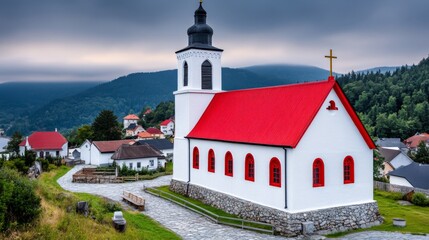 Naklejka premium Scenic view of a white church with a red roof in a rural village surrounded by mountains