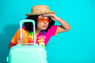 Young woman in a colorful outfit with a suitcase against a bright turquoise background, showing...