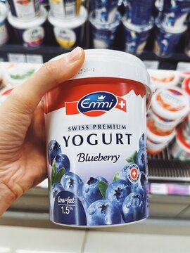 Emmi Swiss Premium Yogurt in blueberry flavor, shown in a round container with vivid fruit imagery. Held in front of a refrigerated display. Swiss dairy. Malaysia, Kuala Lumpur- May, 2025