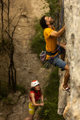 A man is climbing a rock wall while a woman watches