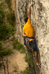 A man is climbing a rock wall wearing a yellow shirt and blue shorts