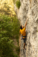 A man in a yellow shirt is climbing a rock wall