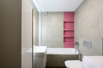 modern bathroom with beige tiles, a white bathtub and sink, and a vertical pink tiled section with shelves