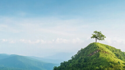 Lone tree stands atop lush green hill, surrounded by rolling mountains and clear blue sky with soft clouds, evoking sense of serenity and solitude