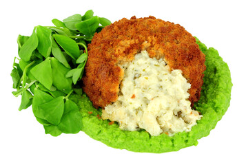 Breadcrumb covered fish cake filled with cod and creamy mashed potato with vivid green pea puree and pea shoot salad leaves isolated on a white background