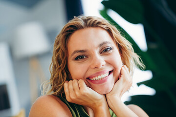 A happy young woman smiling at home in a stylish interior setting, enjoying a comfortable and relaxed moment indoors.