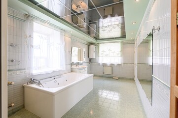 Bright bathroom with a bathtub, tiled walls, and a mirrored ceiling. Features windows with sheer...