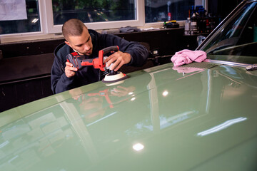 Young man using professional buffer tool to polish car