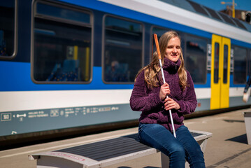 Portrait of blind woman with white cane sitting on train station outdoors in city