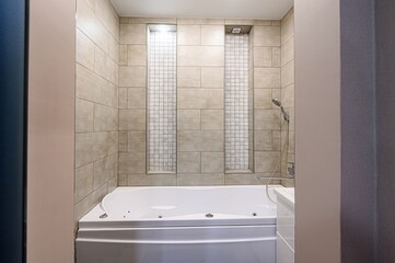 Modern bathroom with a white jacuzzi tub surrounded by tan tiles and decorative tiled niches