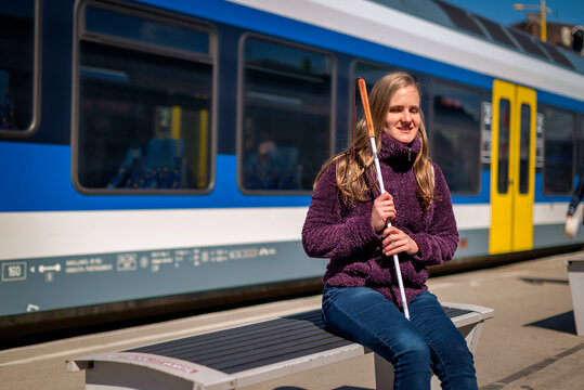 Portrait of blind woman with white cane sitting on train station outdoors in city