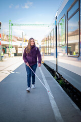 Portrait of blind woman with white cane walking on train station outdoors in city