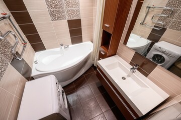 Bathroom featuring a white tub, sink vanity, and washing machine. The room has brown and beige tiles