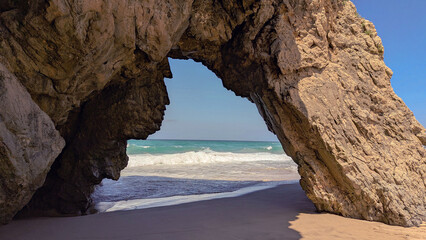 Majestic Arch Rock Formation Framing Ocean Waves and Sandy Beach on a Sunny Day. Seascape.