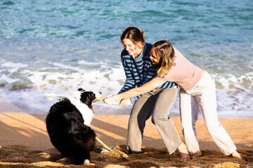 Mother and daughter playing tug-of-war with border collie on Costa Brava beach