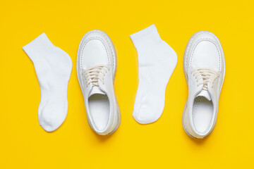 Casual female leather shoes with white socks top view on yellow background, stylish footwear.