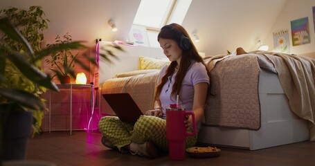 Daytime leisure of a teenage girl. She uses a laptop and eats snacks while sitting on the bedroom...