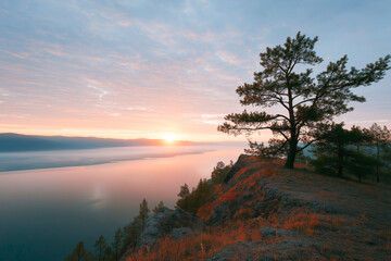 Scenic sunrise over tranquil lake with silhouetted trees on cliffside