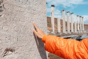 Tourist pointing finger at ancient greek inscription carved on a marble stone