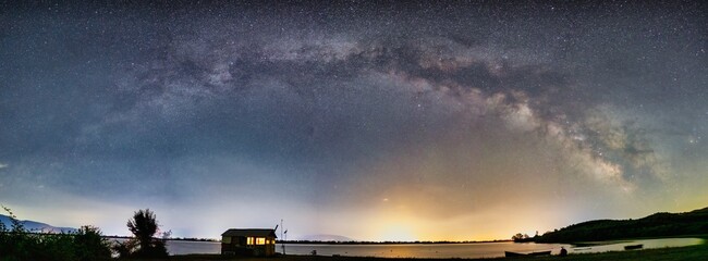 A tranquil night at Lake Kerkini, where a wooden cabin glows warmly under a breathtaking Milky Way, Greece