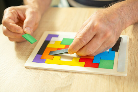 senior man's engaged hands skillfully maneuver colorful wooden pieces brain teaser puzzle, highlighting importance mental stimulation