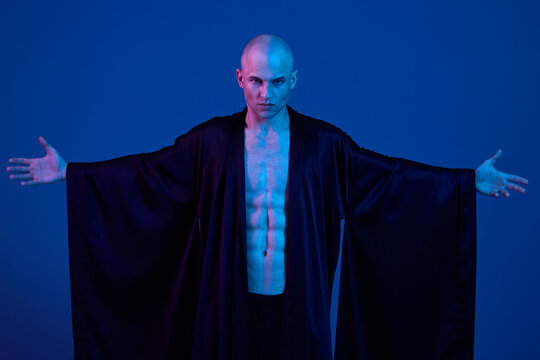 Fototapeta Confident man in dark robe, showcasing strength with blue lighting. Perfect for artistic and dramatic compositions, emphasizing bold expressions and contrast.