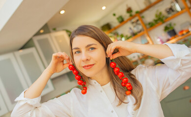 Light-Skinned European Woman Smiling with Cherry Tomatoes Held Like Earrings in Bright Home Kitchen
