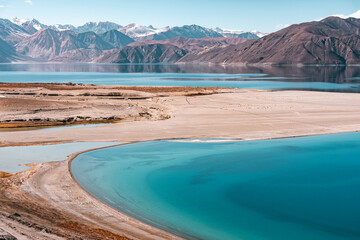 Scenic view of Pangong Lake surrounded by majestic brown mountains under a clear blue sky, reflecting pristine waters, creating a serene and picturesque high-altitude Himalayan landscape in Ladakh