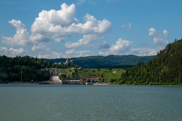 Fototapeta premium Hydroelectric dam and power station near Niedzica Castle in southern Poland, surrounded by forested hills and a lake on a sunny day.