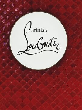 Circular white Christian Louboutin sign on glossy red textured wall with scale-like tile pattern. Black handwritten-style logo in center.High-end shoes.Malaysia, Kuala Lumpur- May, 2025